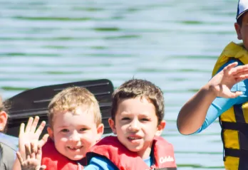 image of young kids waving from a canoe