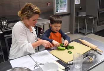 mother teaching young son how to cut a pepper during cooking class