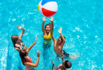 overhead image of kids in bright blue pool jumping for a beach ball