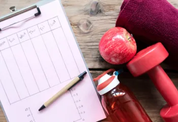 image of workout plan, apple, dumbbell, water bottle, and towel