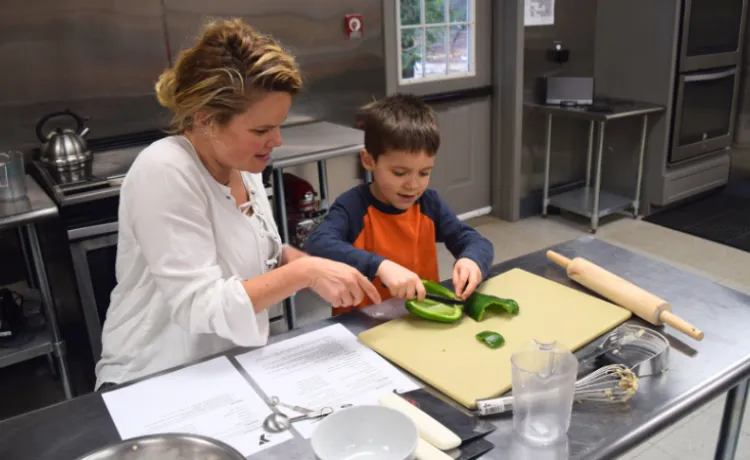 mother teaching young son how to cut a pepper during cooking class