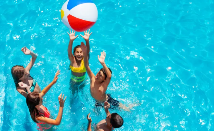 overhead image of kids in bright blue pool jumping for a beach ball