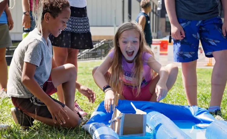 photo of boy and girl racing their cardboard boat