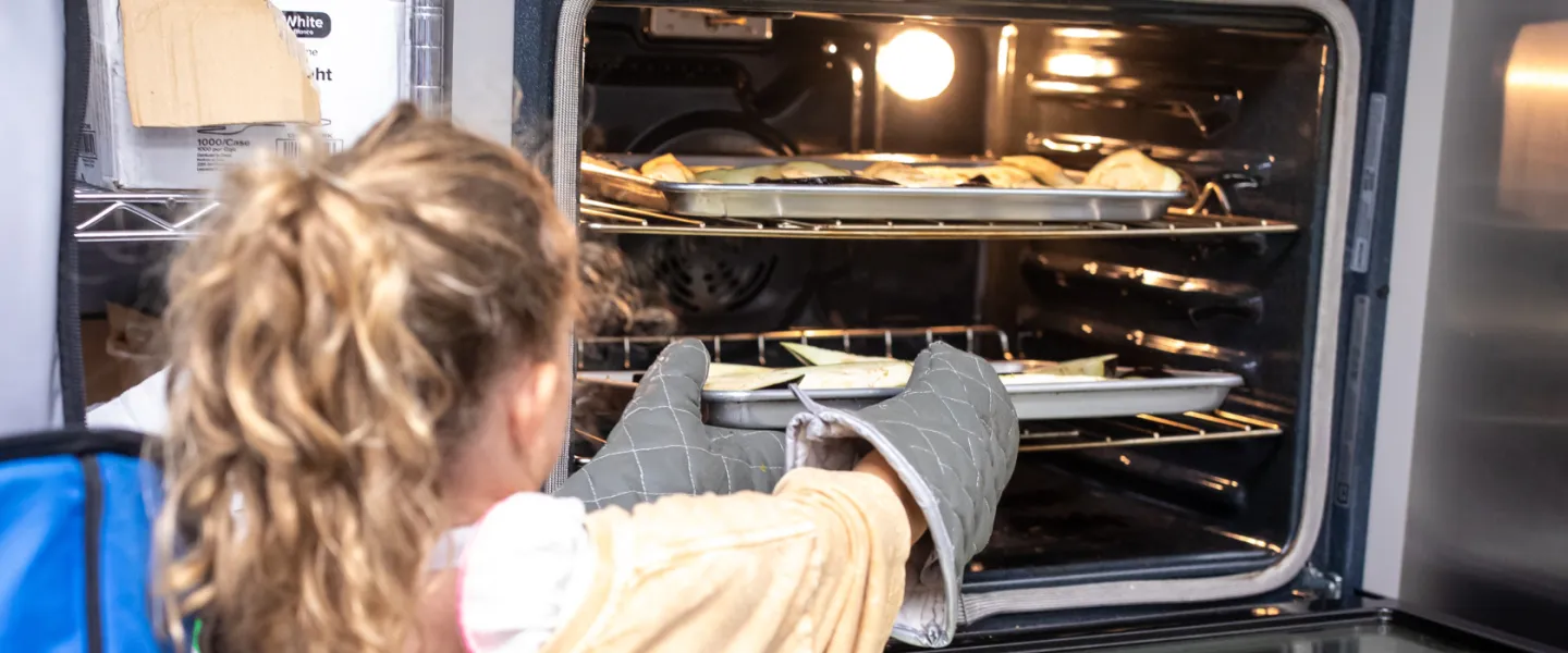 girl in kitchen removing food from oven