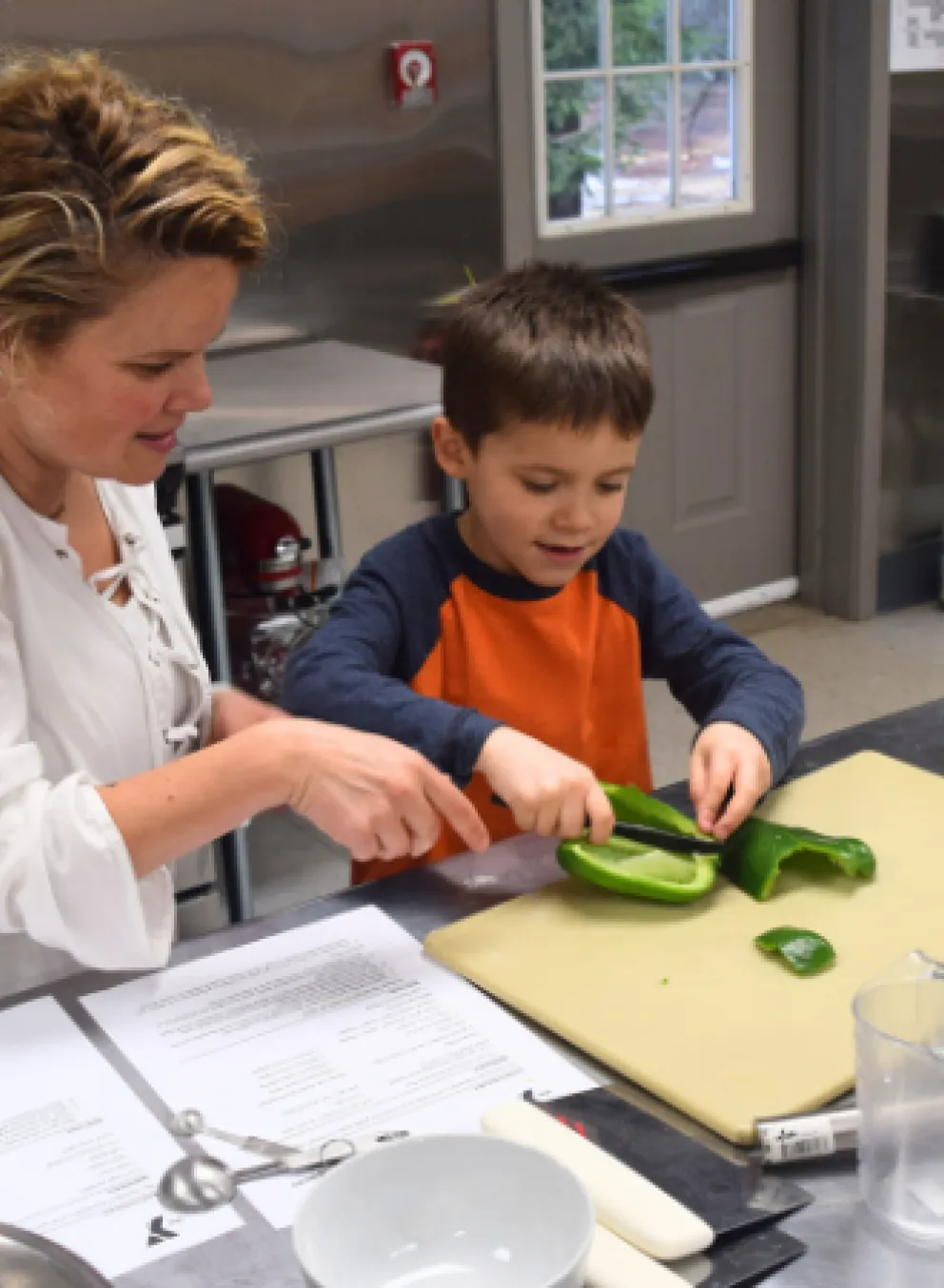 mother teaching young son how to cut a pepper during cooking class