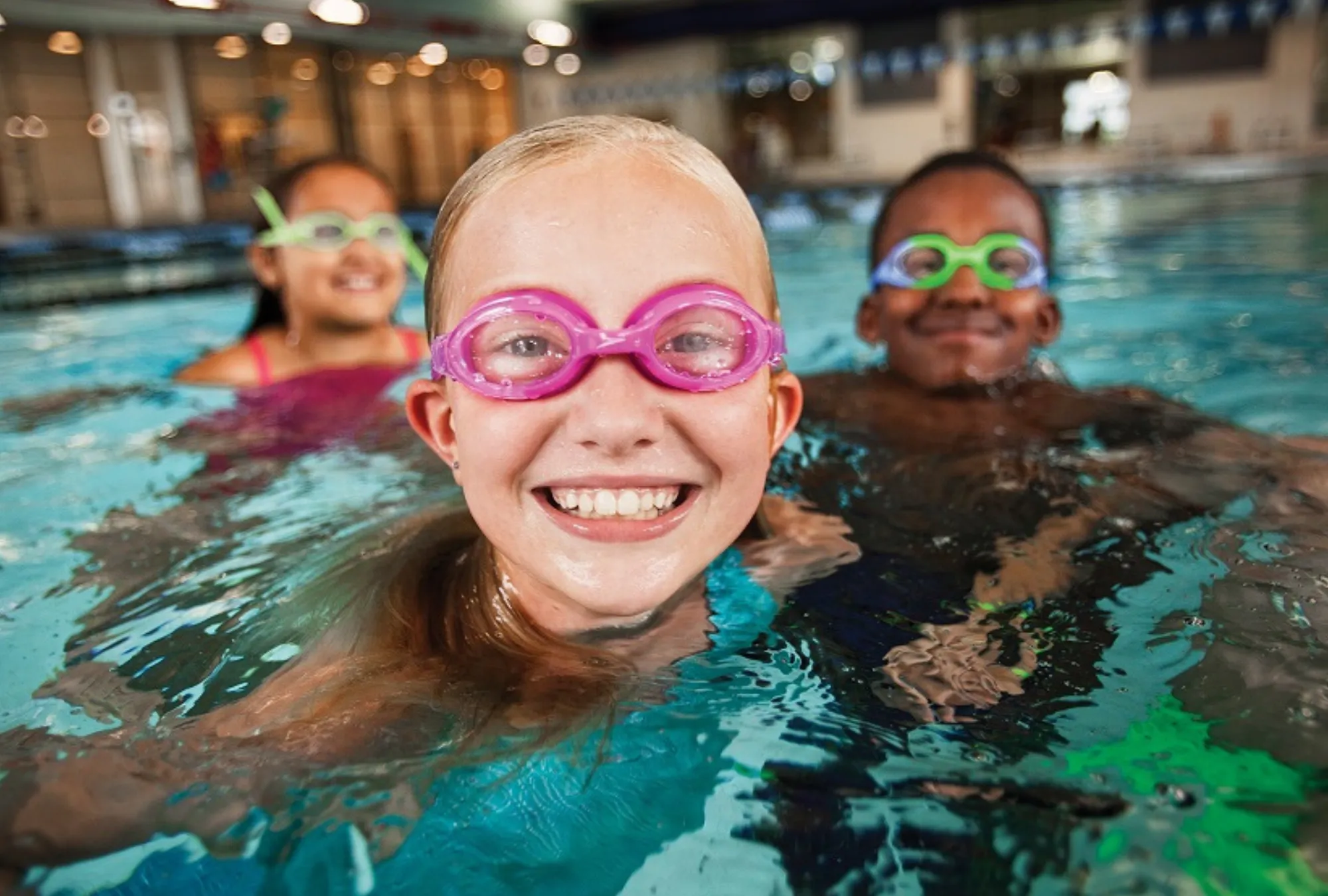 three kids wearing goggles in the pool smiling
