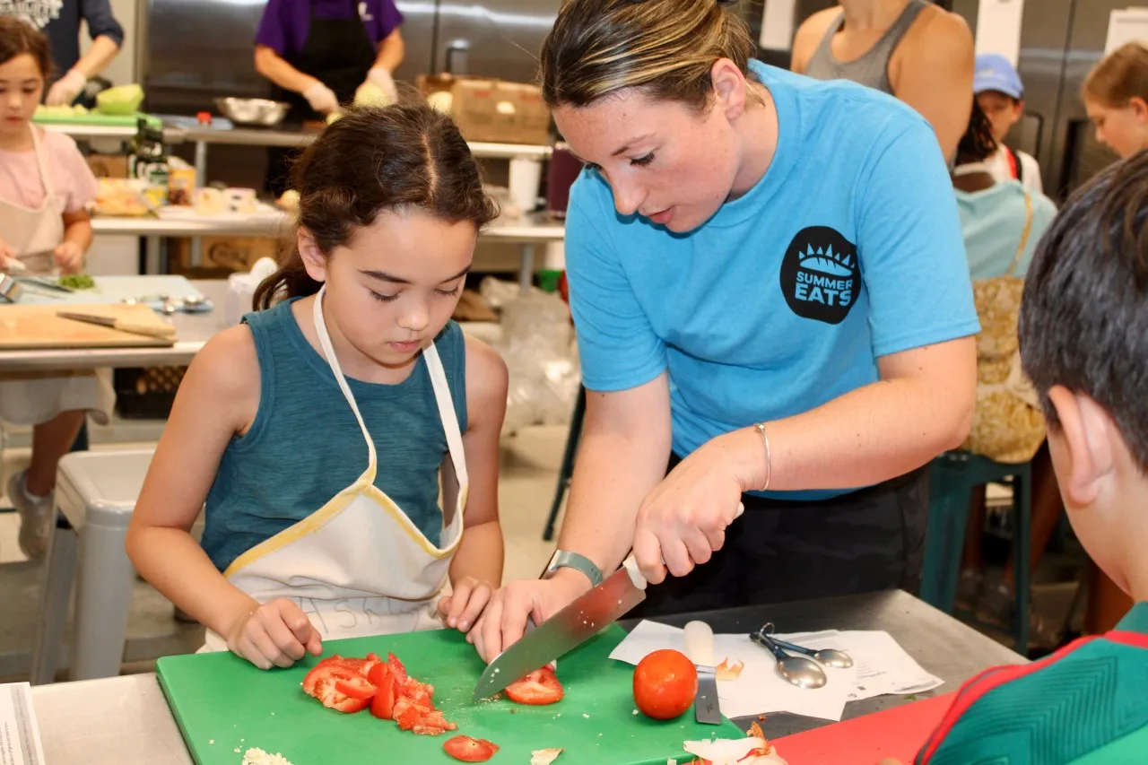 photo of camp staff showing camper how to chop tomatoes