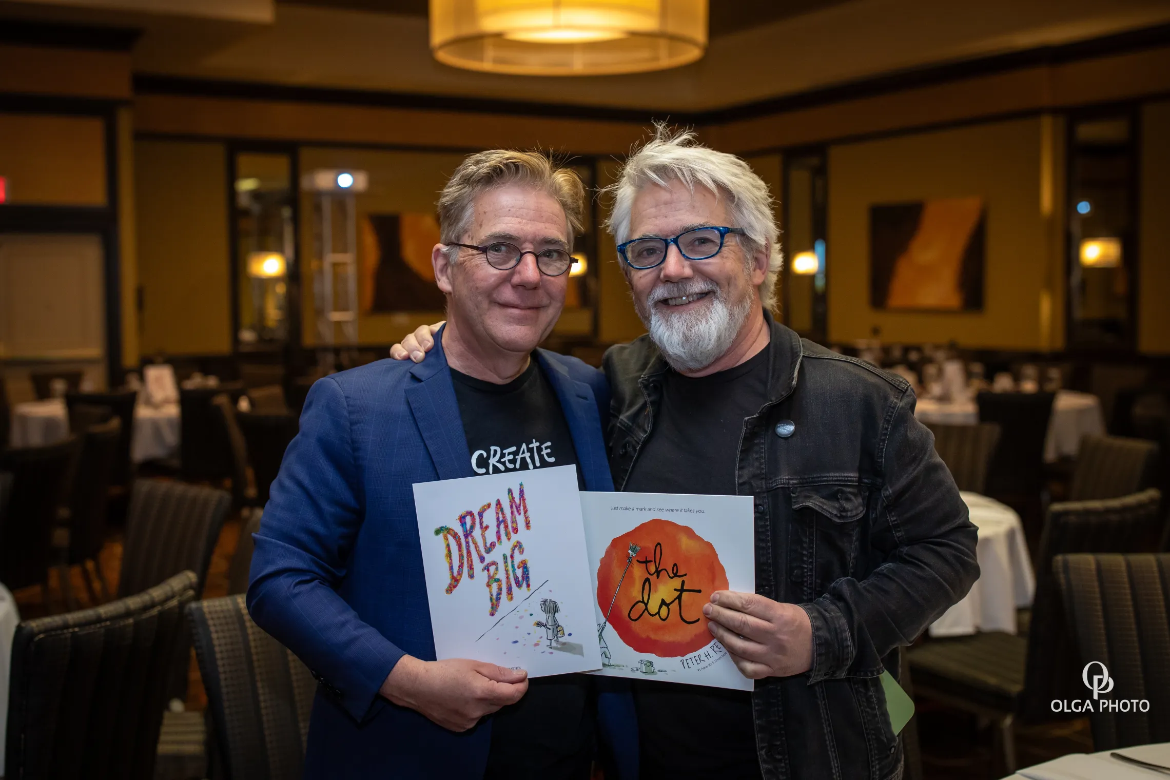 image of two males smiling and holding up a book