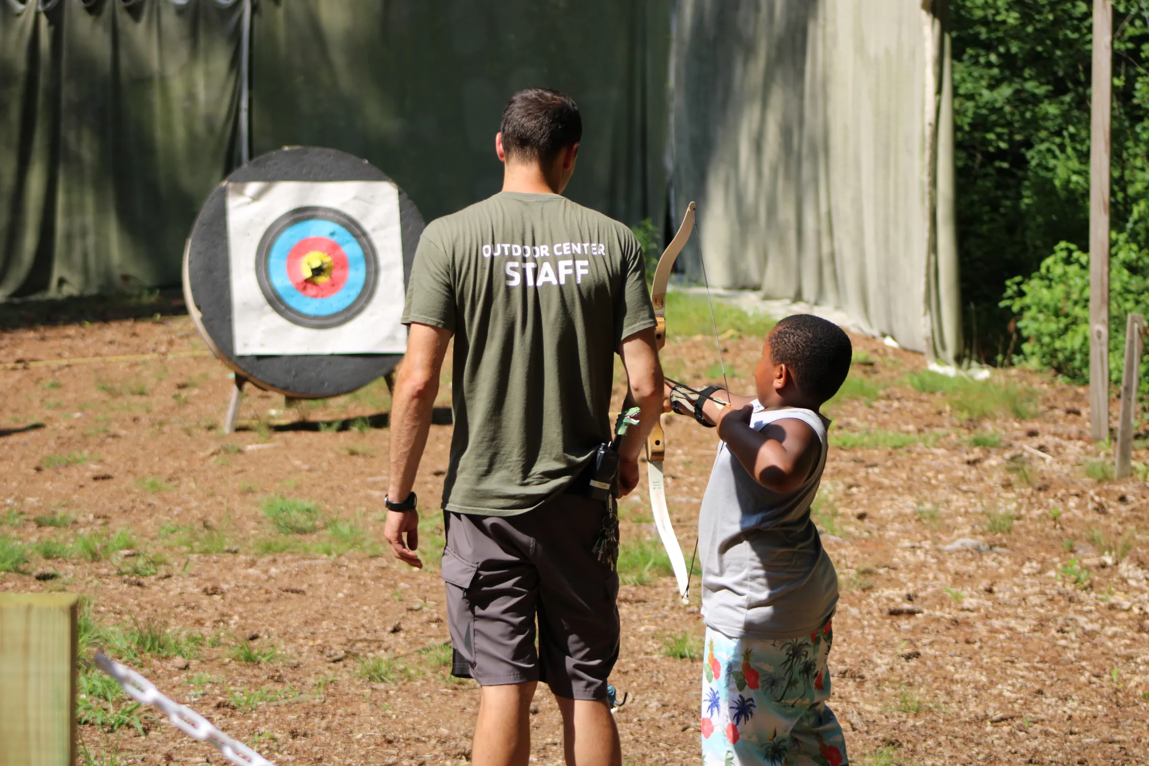 image of camp staff helping young boy at archery range