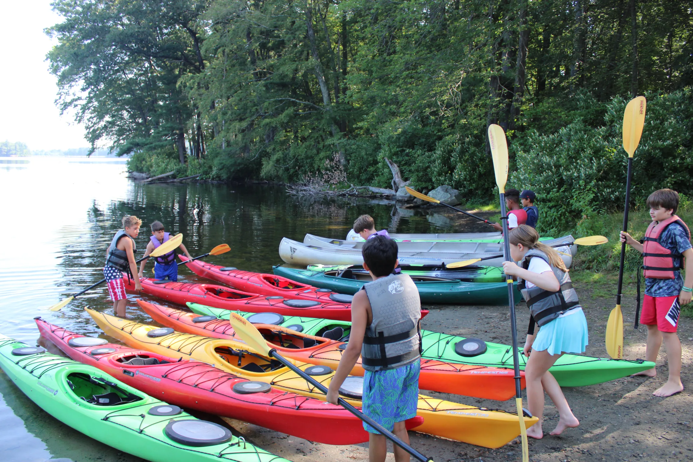 campers wearing life jackets standing next to colorful kayaks