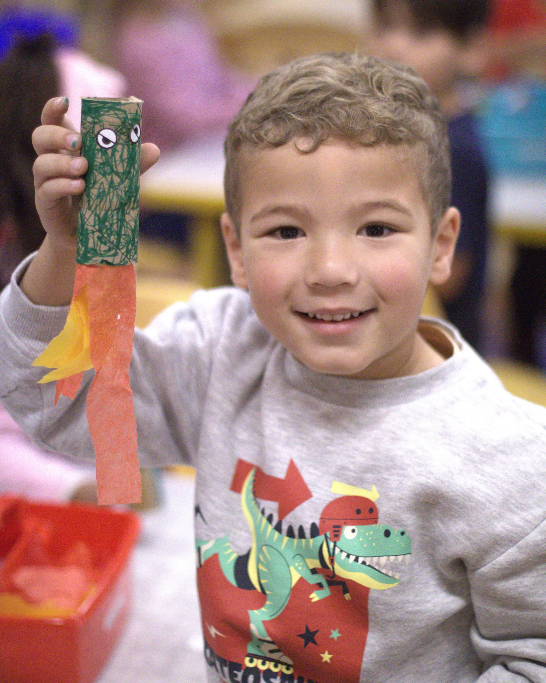 A little boy proudly holds up his art project.