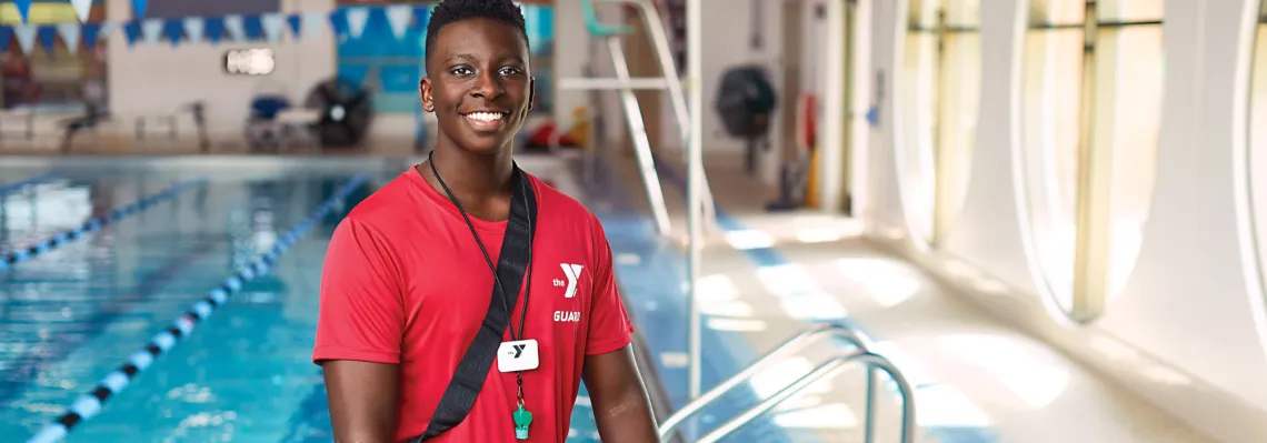 teen lifeguard standing in front of the pool smiling