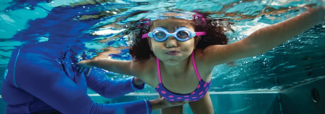 young girl swimming under water wearing goggles