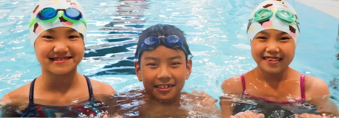 three youth swimmers in the pool smiling