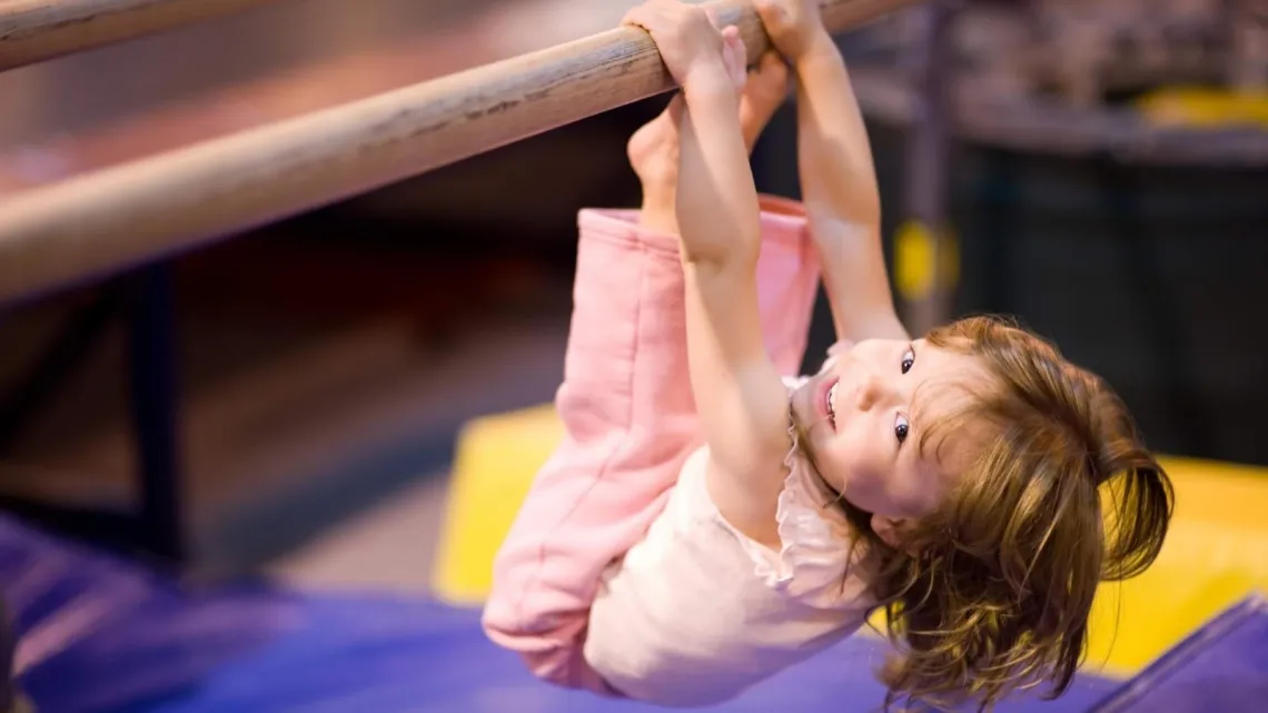 young girl smiling while hanging from balance beam