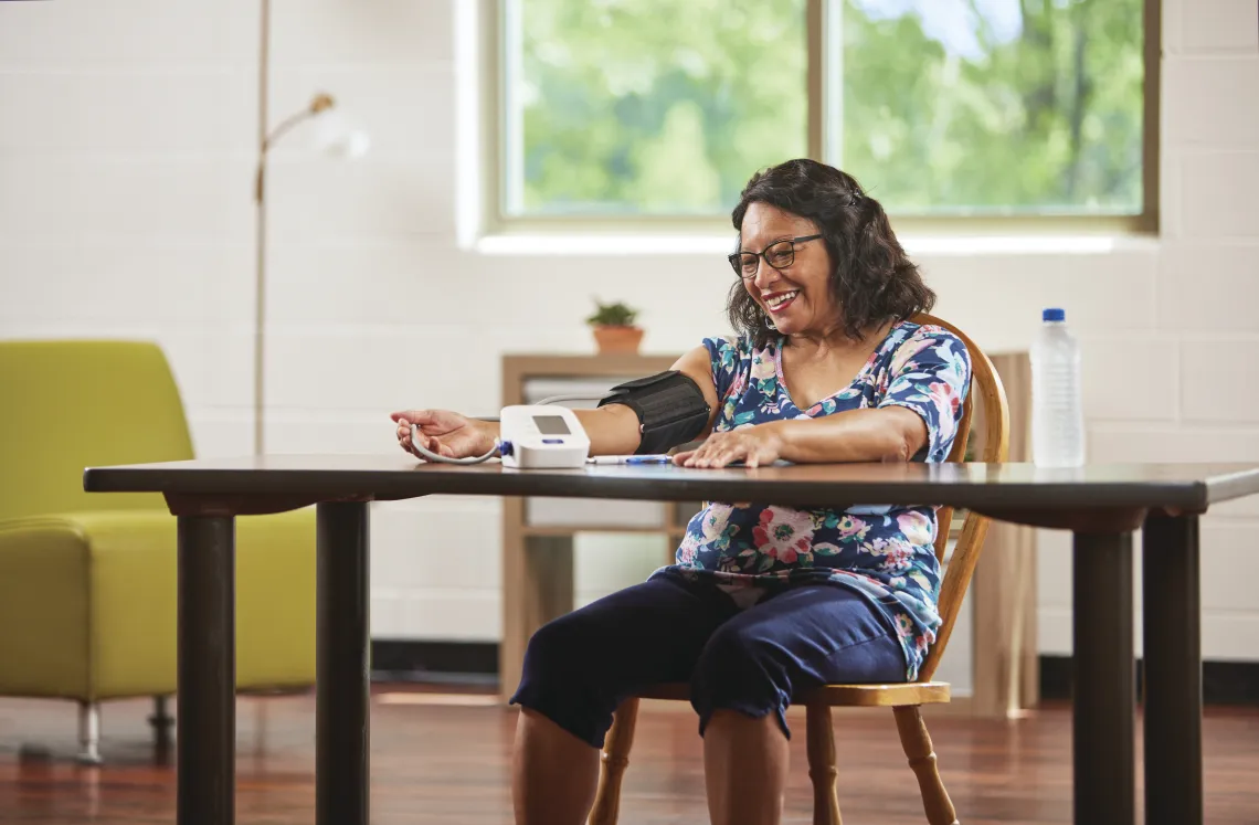 older woman sitting at table taking her blood pressure