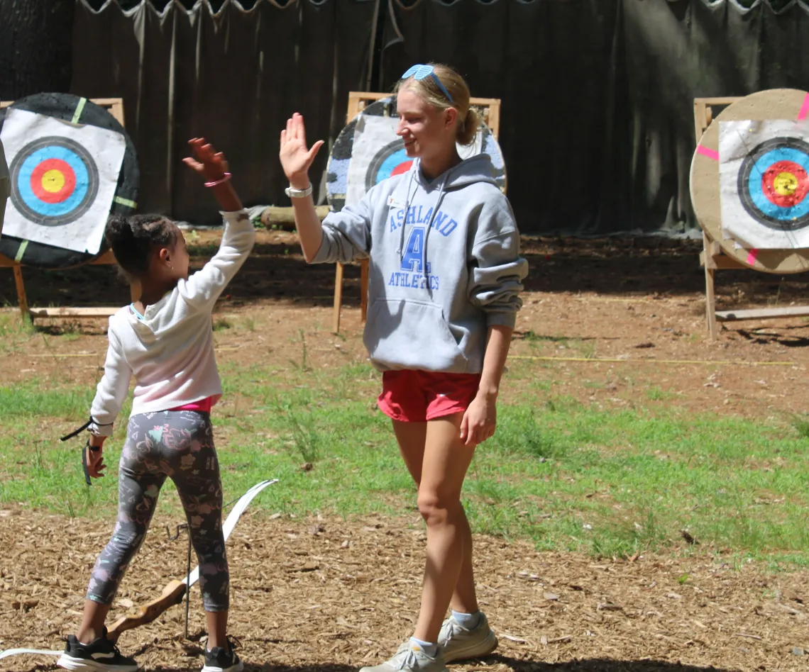 camp counselor and camper high fiving on archery range