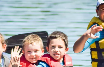 image of young kids waving from a canoe