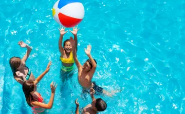 overhead image of kids in bright blue pool jumping for a beach ball